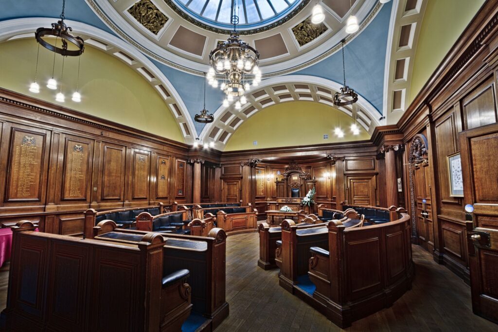 A wood-panelled town hall council chamber under a skylight