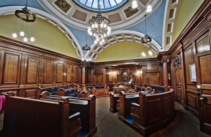 A wood-panelled town hall council chamber under a skylight
