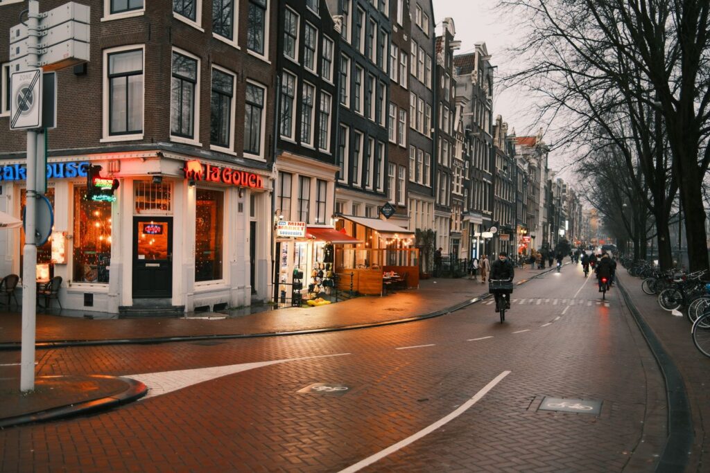 Cyclists on a town street at dusk, shop windows lit