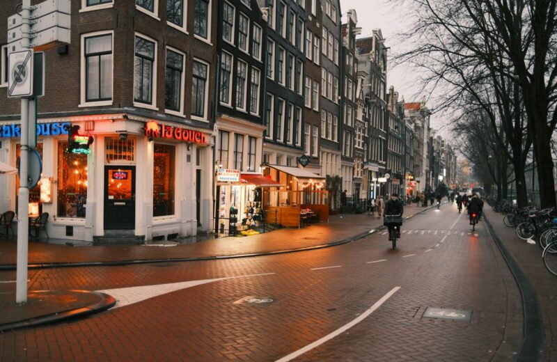 Cyclists on a town street at dusk, shop windows lit