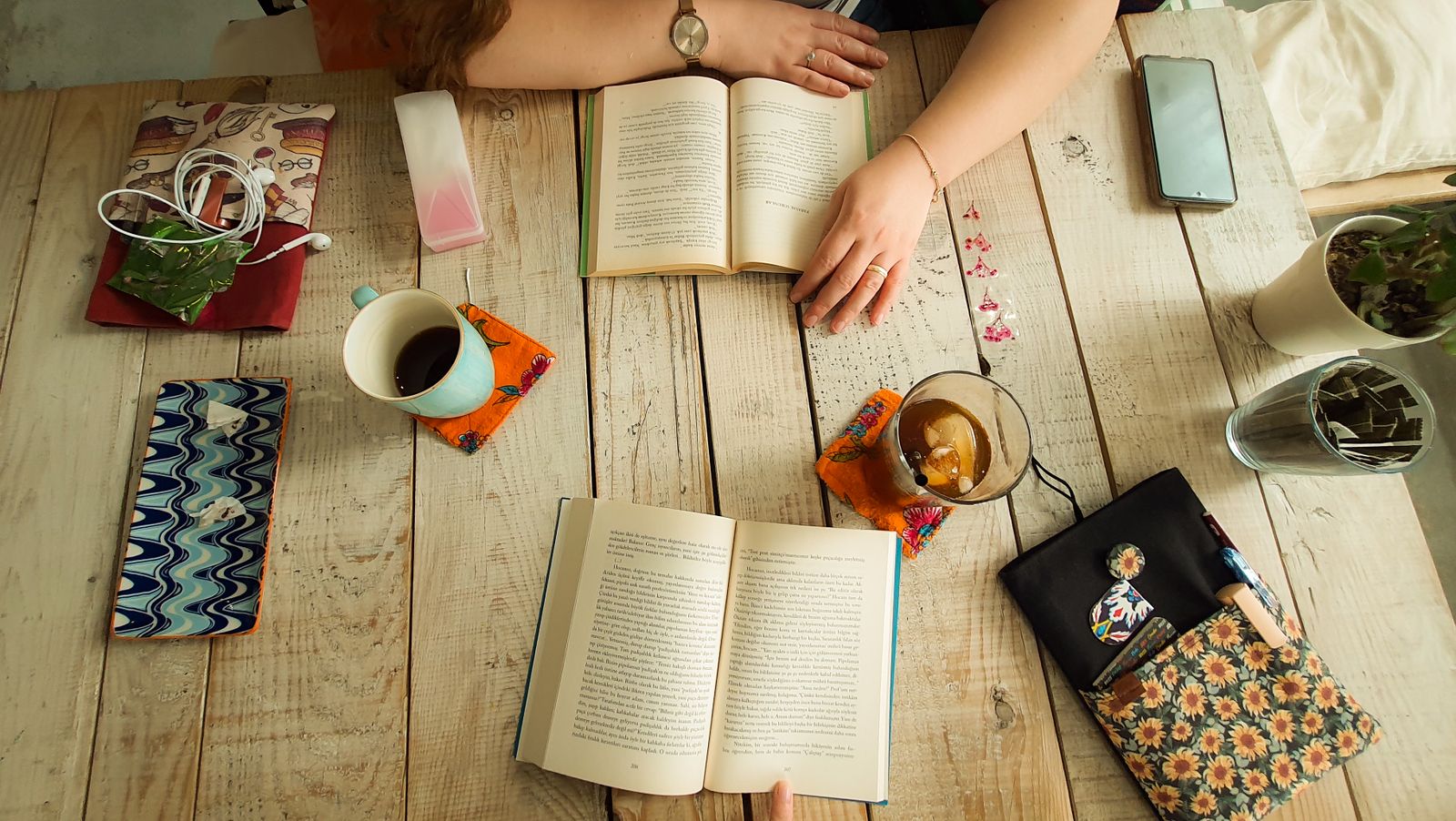 Readers' hands with open books, cups and notes on a rustic wooden table