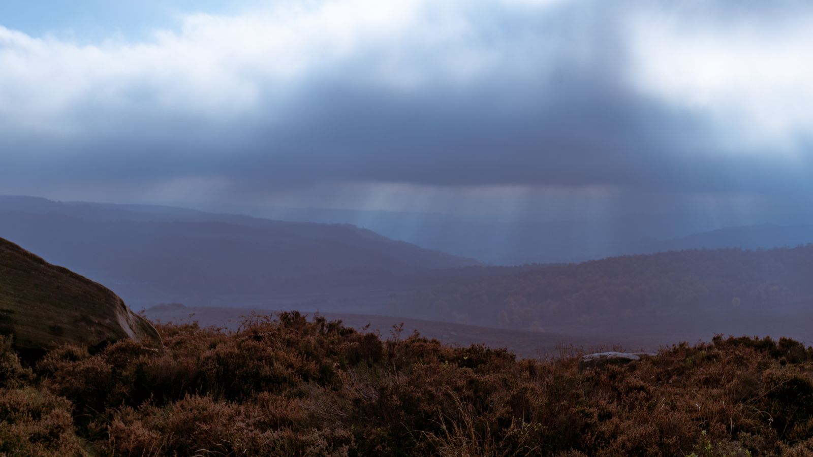 Moorland hills under low rain clouds, with light breaking through