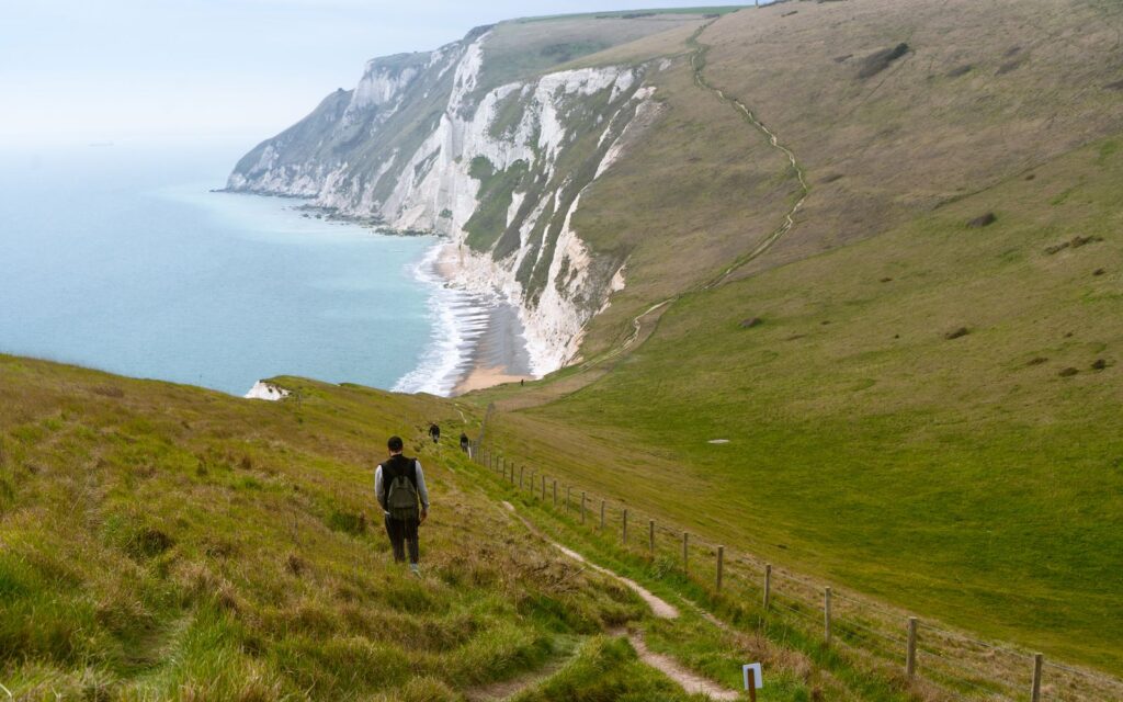 A walker on a grassy cliff path high above the sea