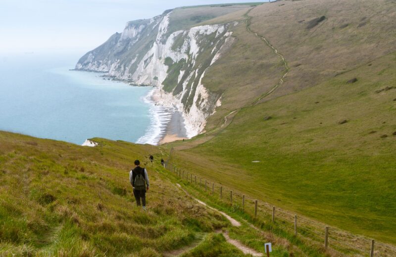 A walker on a grassy cliff path high above the sea