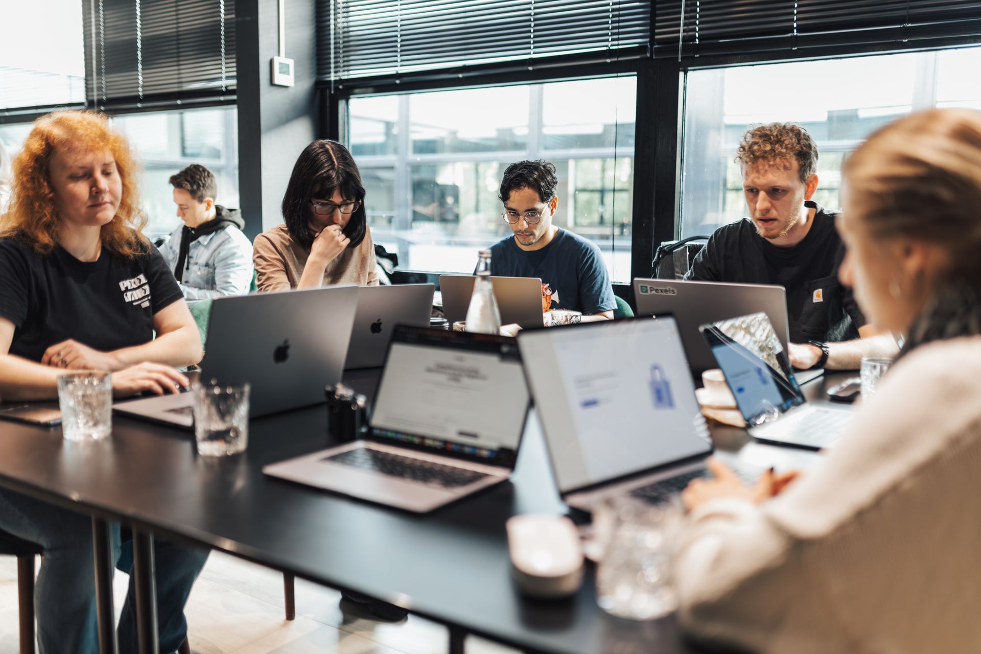 A team of eight around a long meeting table with laptops and notebooks in a bright office