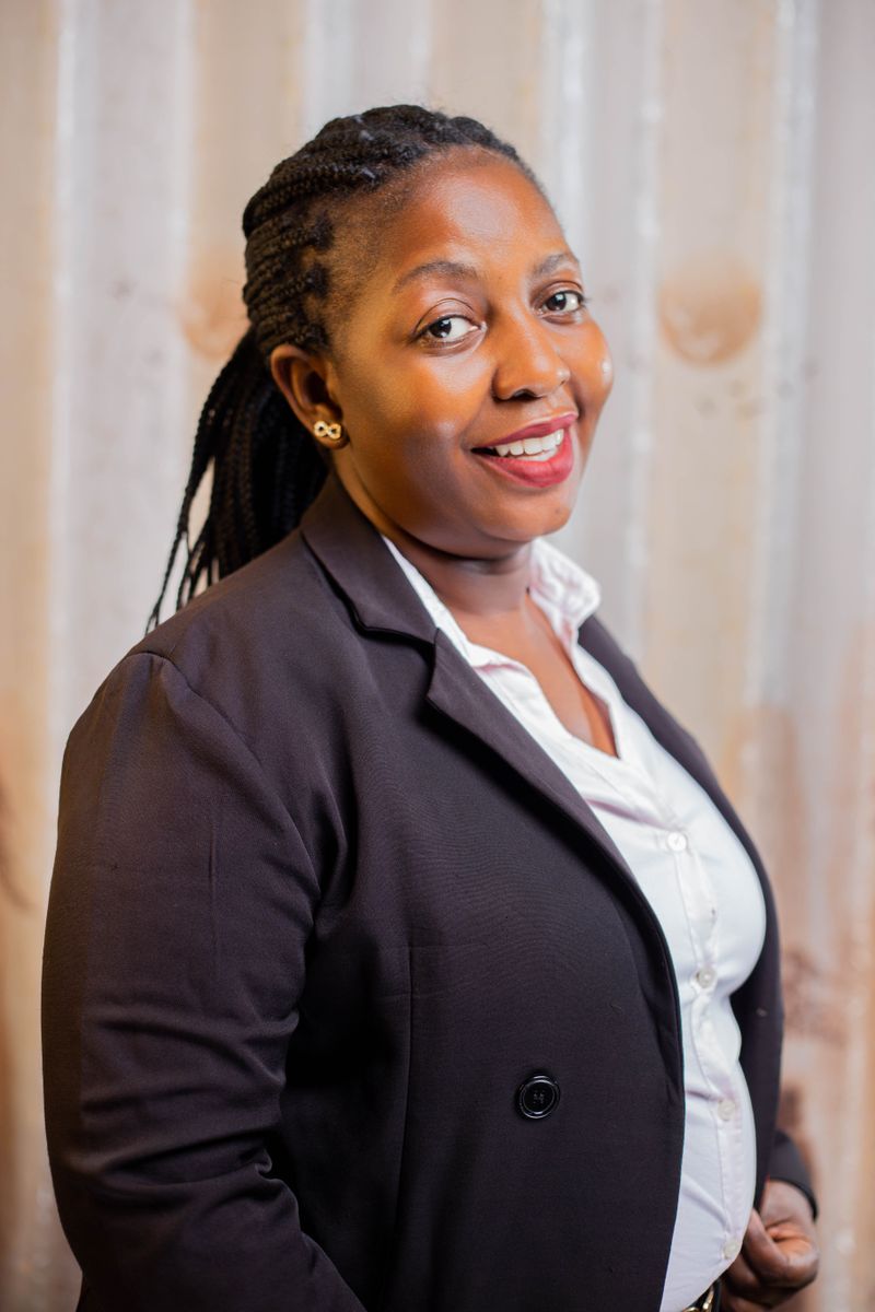 Portrait of a woman with braided hair in a dark blazer, smiling by a window