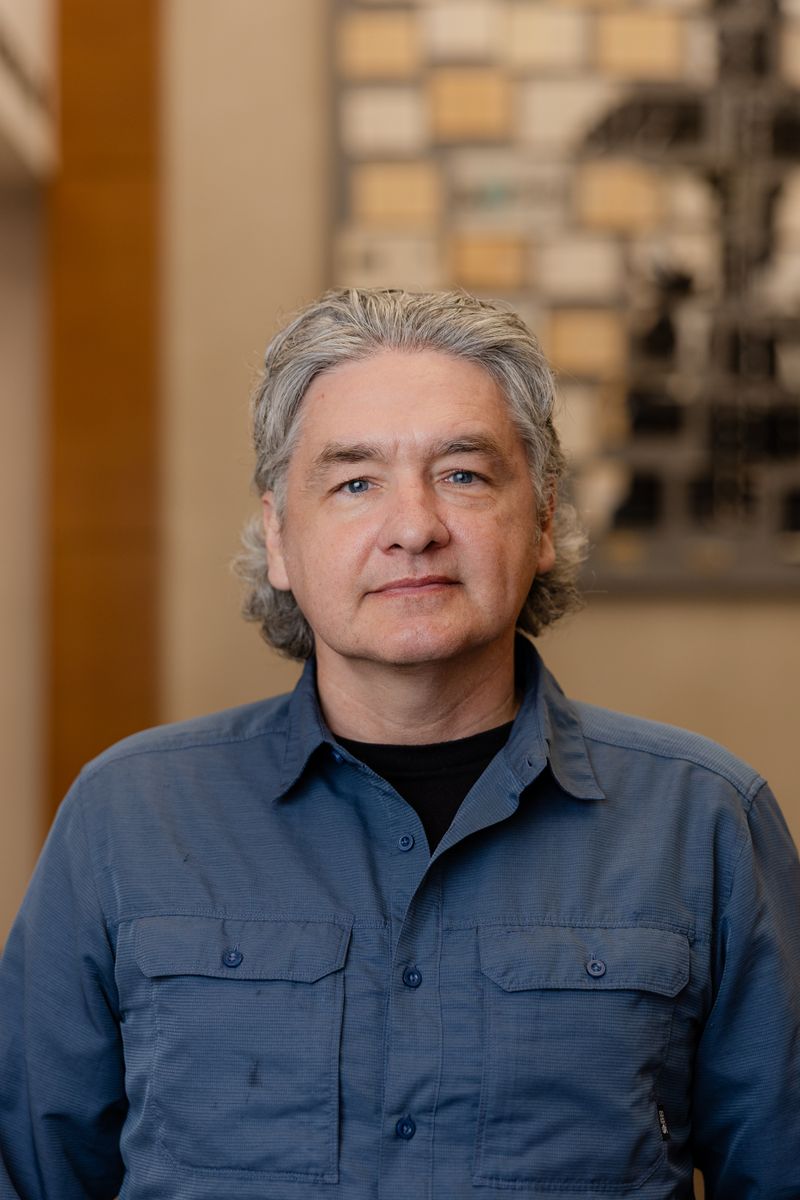 Portrait of an older man with grey hair in a blue shirt in a warm-lit office