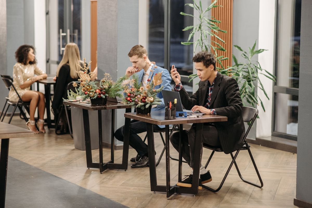 An open office with small tables, plants and people meeting by a big window