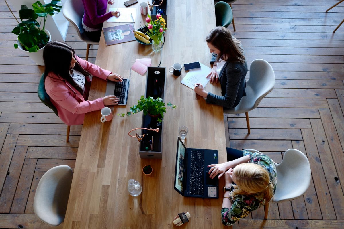 An office seen from above: people working at a long wooden table with laptops