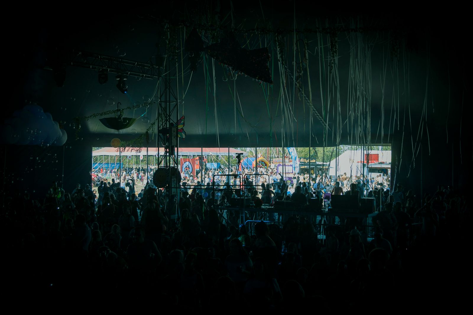 A crowd in silhouette in front of an open-air stage lit in pink and purple