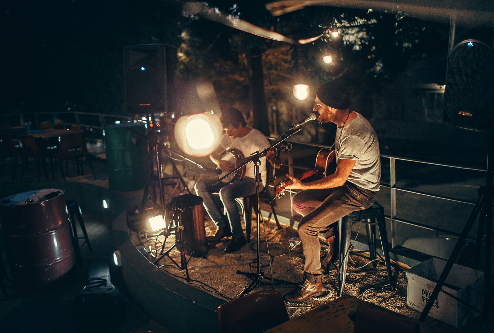 Two musicians playing an acoustic set outdoors under warm evening lights