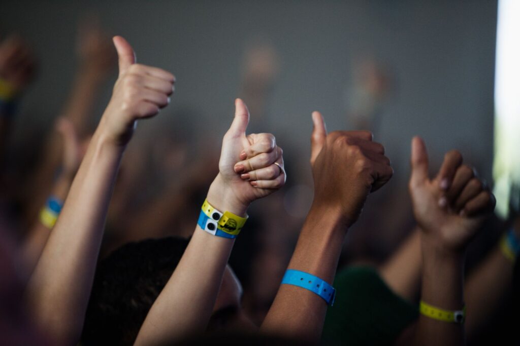 Raised hands giving a thumbs up, with festival wristbands on the wrists