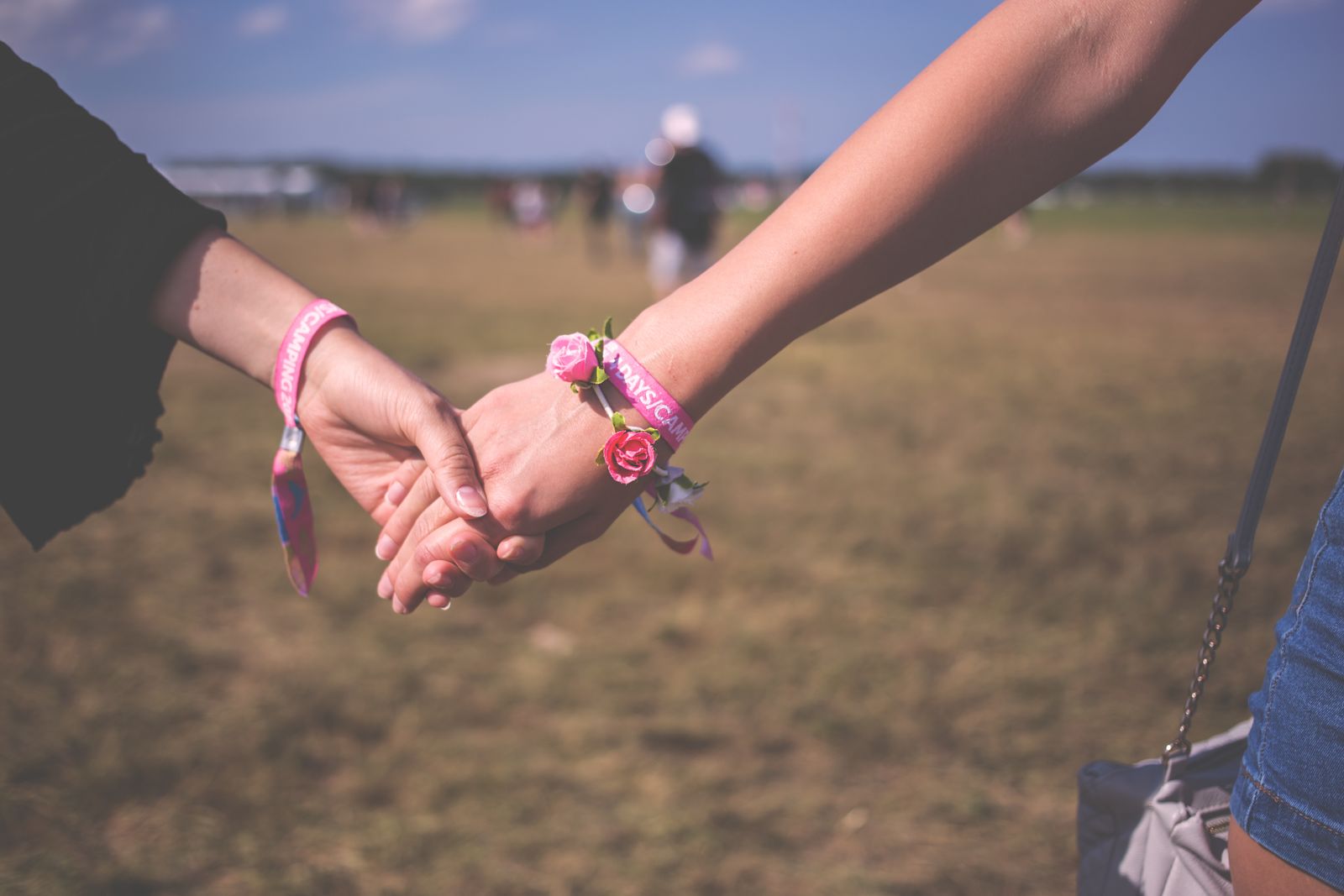 Two friends holding hands, both wearing festival wristbands
