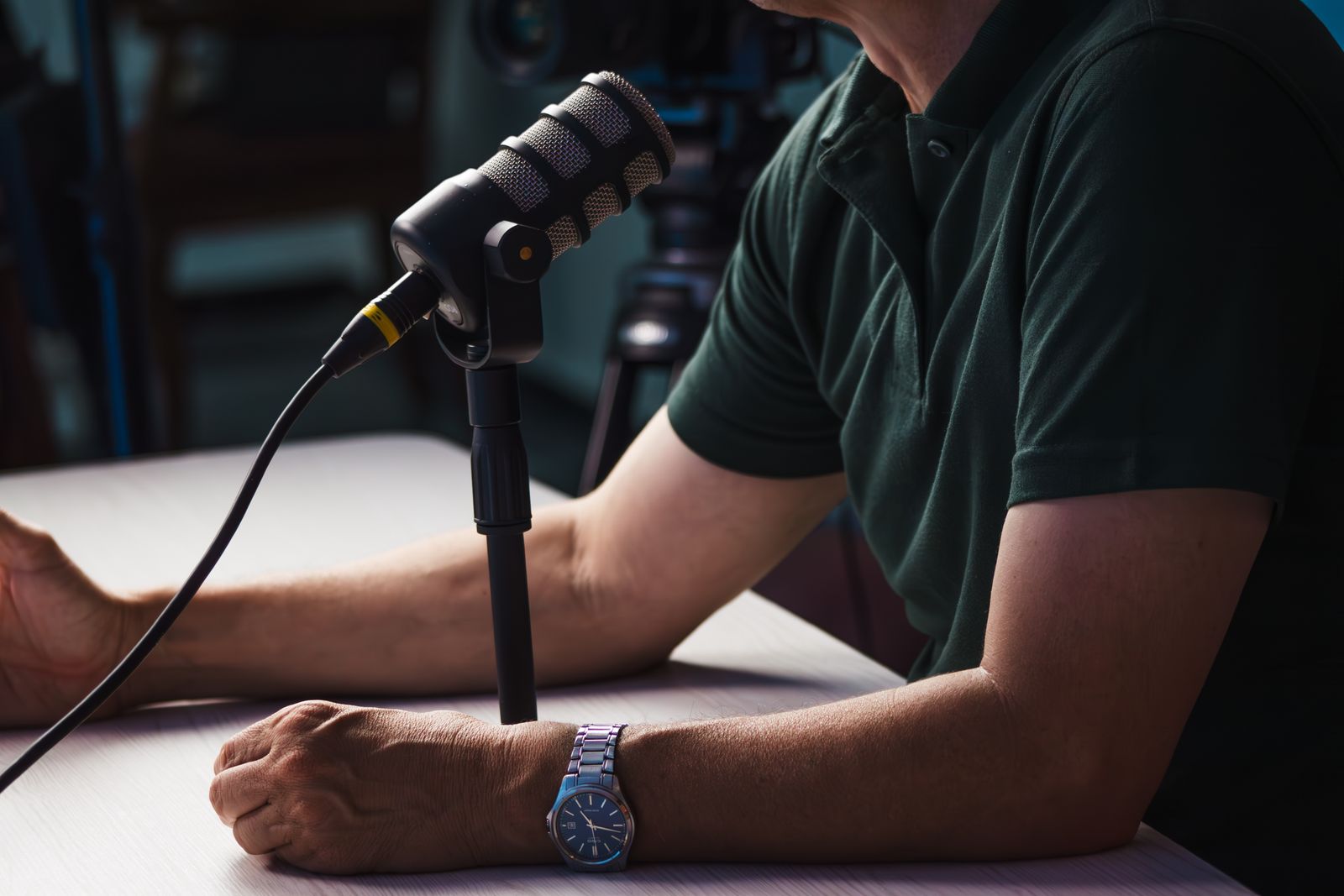 A person speaking into a microphone at a table during a recorded interview