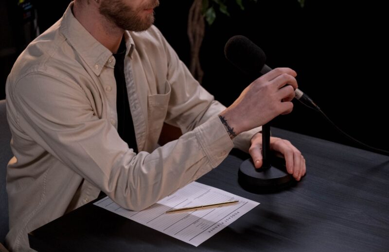 A man answering questions at a microphone with notes in front of him