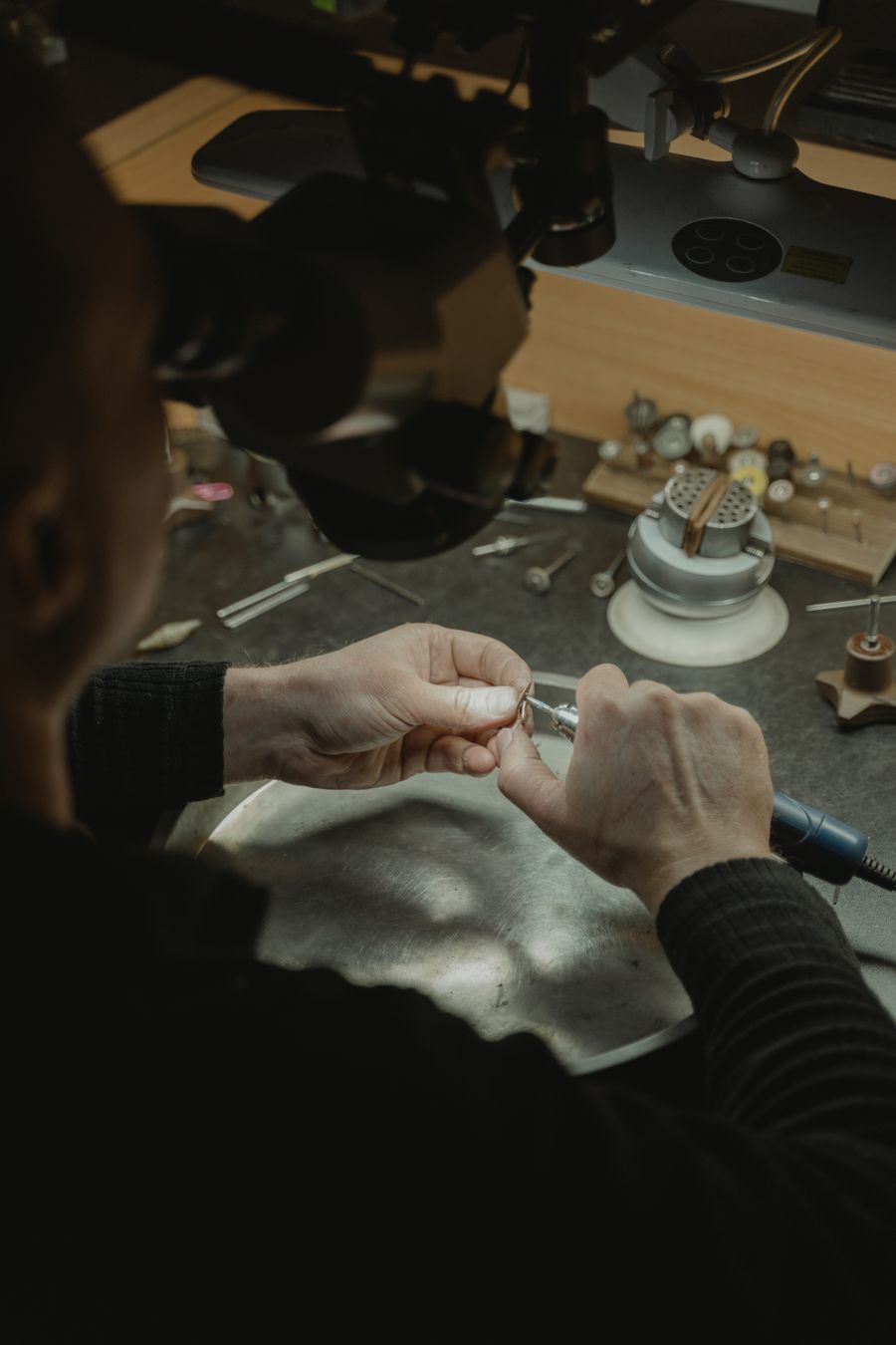 A jeweller's hands at a workbench, working on a small piece with fine tools