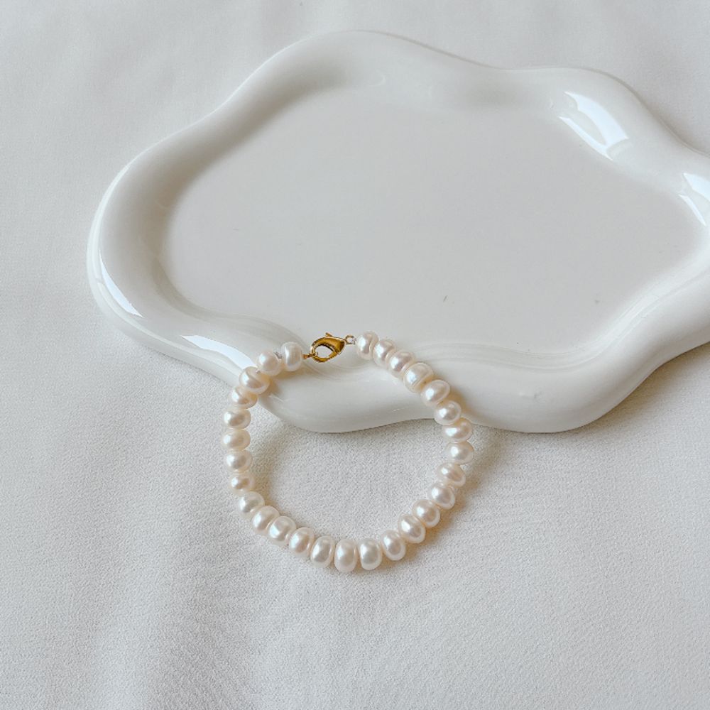 A freshwater pearl bracelet with a gold clasp on a curved white ceramic dish