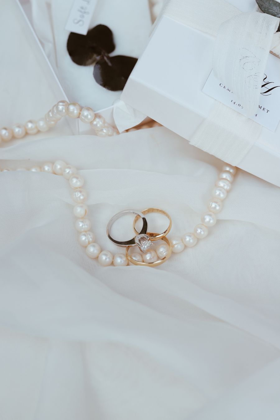A pearl strand and two gold rings laid on white fabric