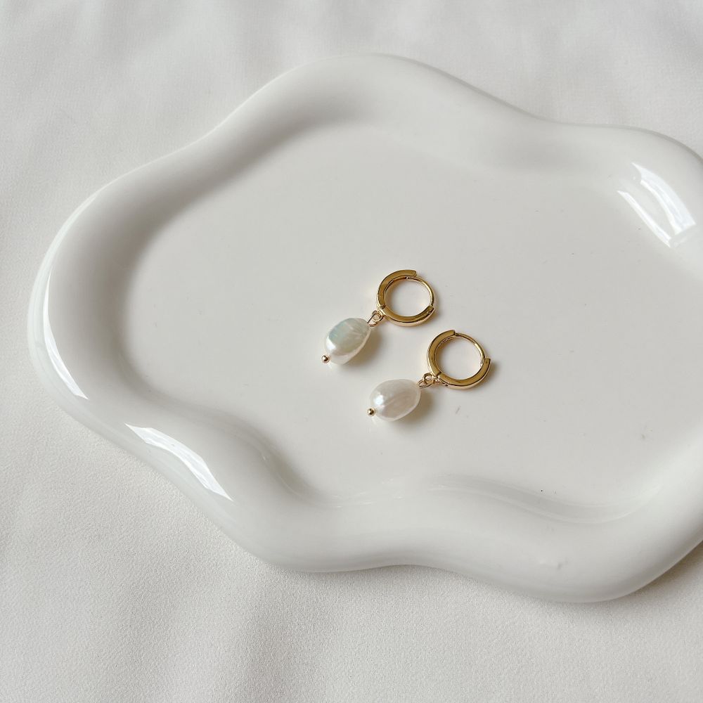 A pair of small gold hoop earrings with pearl drops on a white ceramic dish