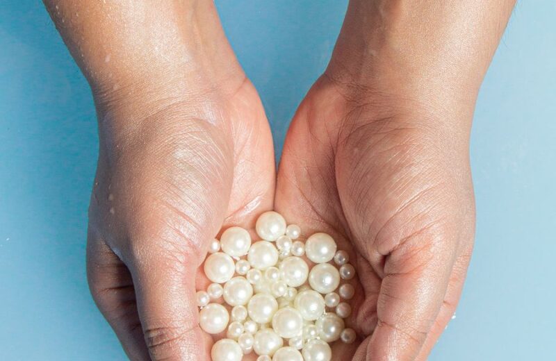 Cupped hands holding a heap of white pearls against a soft blue background