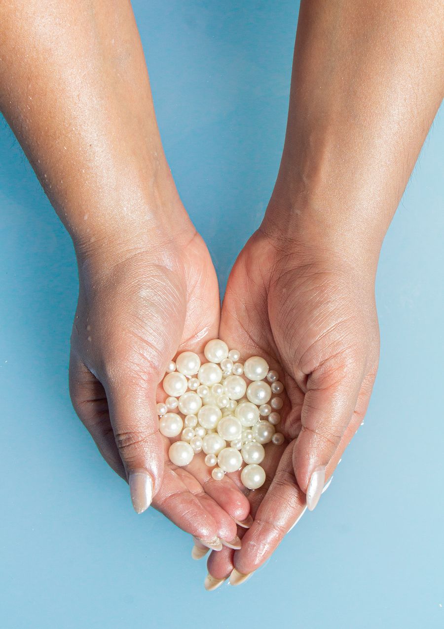 Cupped hands holding a heap of white pearls against a soft blue background