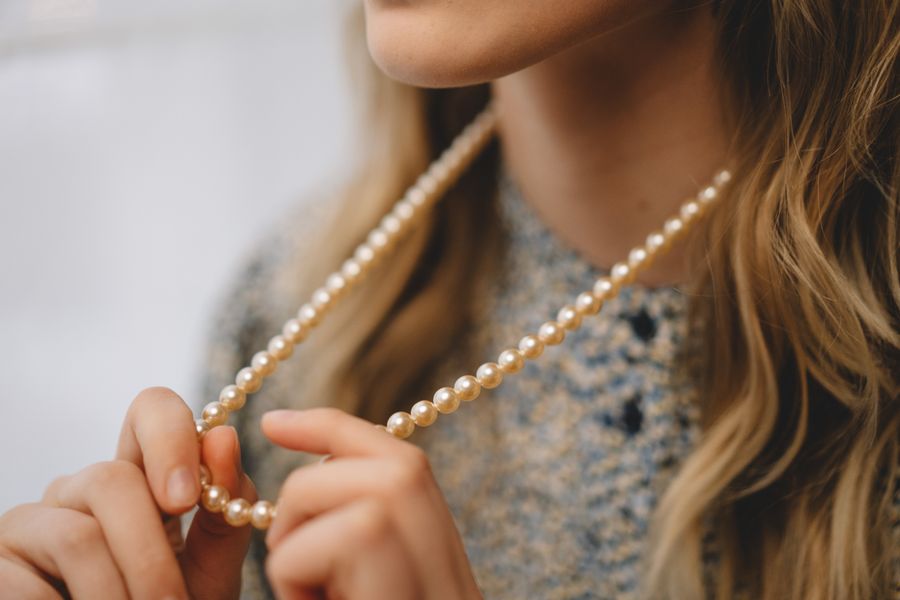A hand holding up a long pearl necklace with a pearl pendant