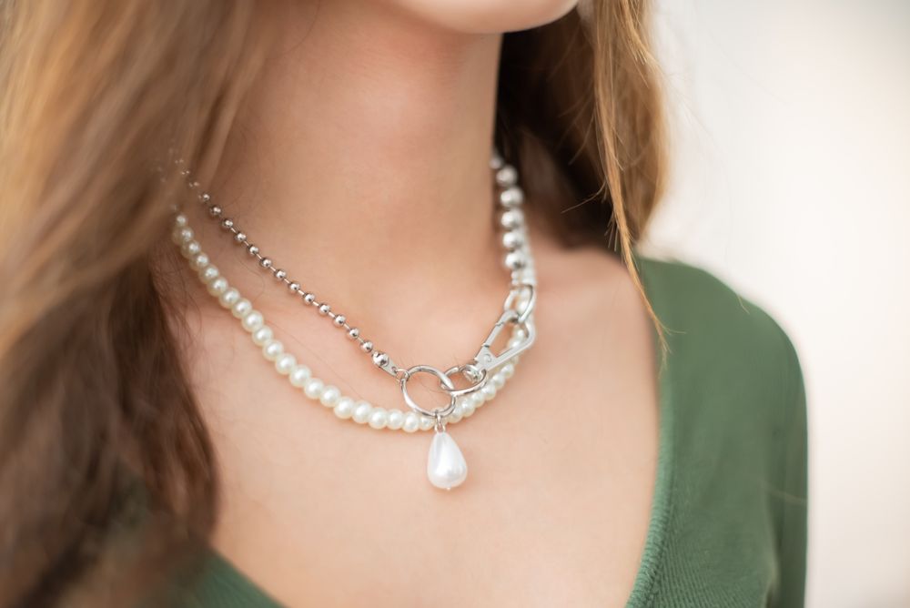 Layered pearl necklaces with a silver chain and a drop pearl, worn with a green top