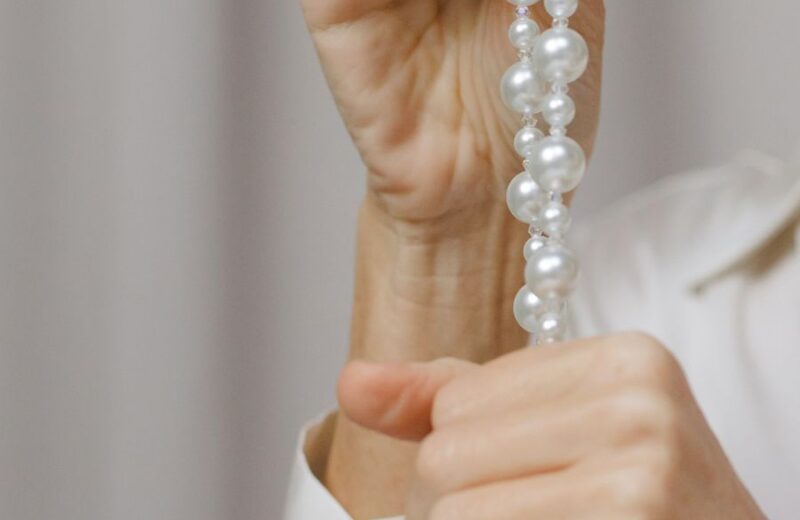 Two hands holding a strand of round white pearls
