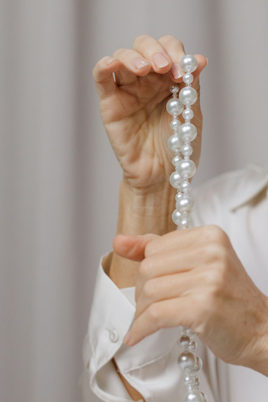 Two hands holding a strand of round white pearls