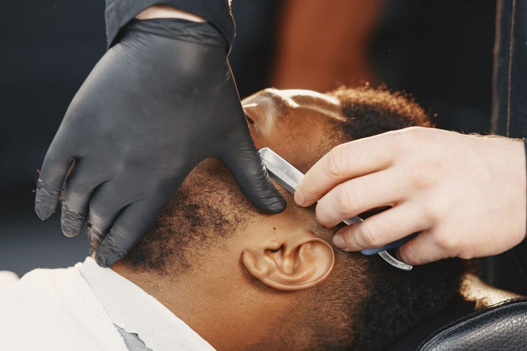 A barber in black gloves lining up a beard with a razor