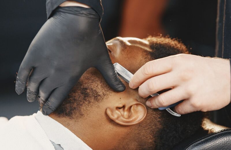 A barber in black gloves lining up a beard with a razor