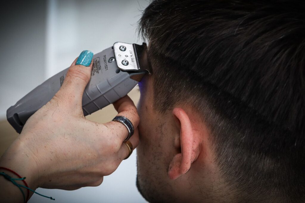 A barber's hand guiding clippers above a client's ear