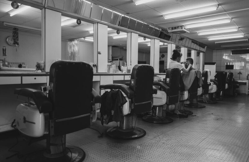 A long row of barber chairs and mirrors, in black and white