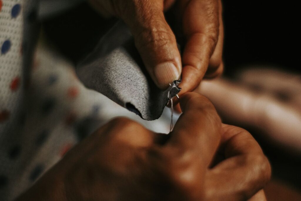 Hands sewing grey fabric with a needle and thread