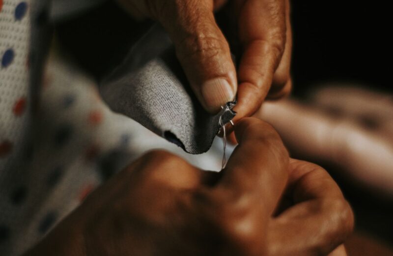Hands sewing grey fabric with a needle and thread