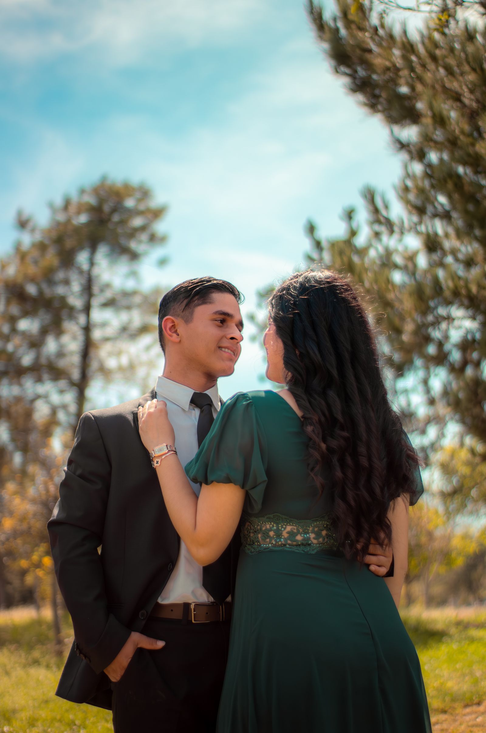 A couple embracing outdoors in sunlight, trees behind them