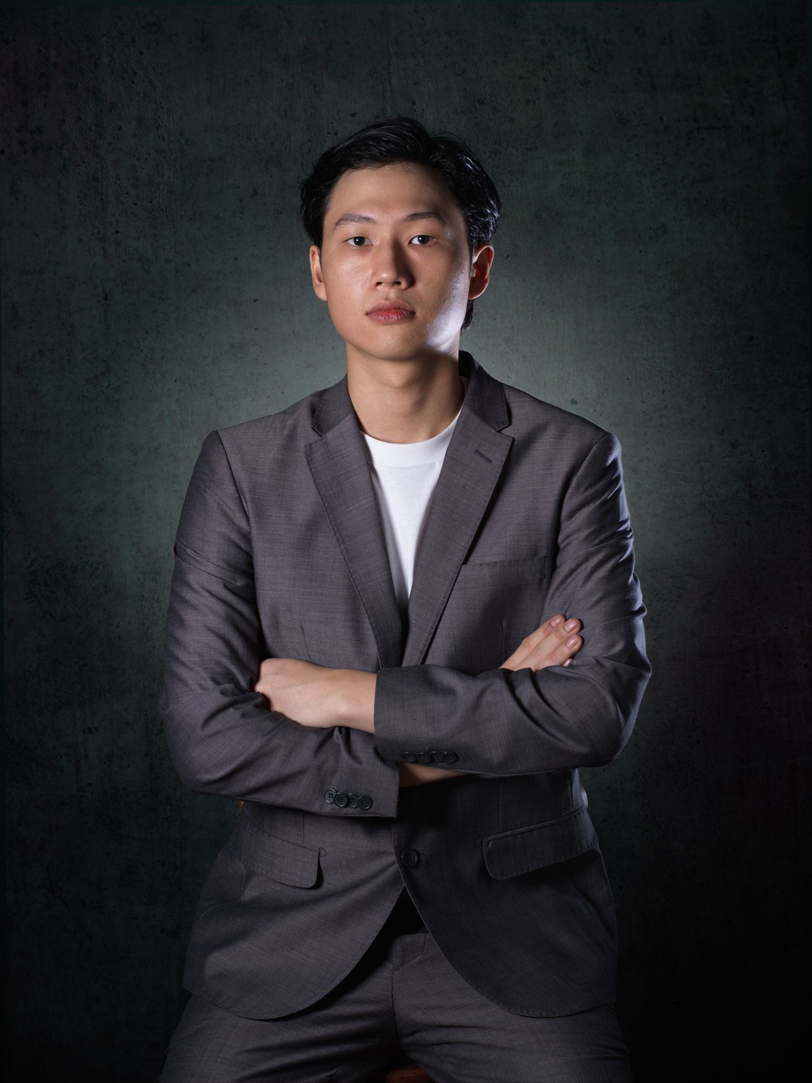 Headshot of a man in a grey suit with arms folded, on a dark grey background