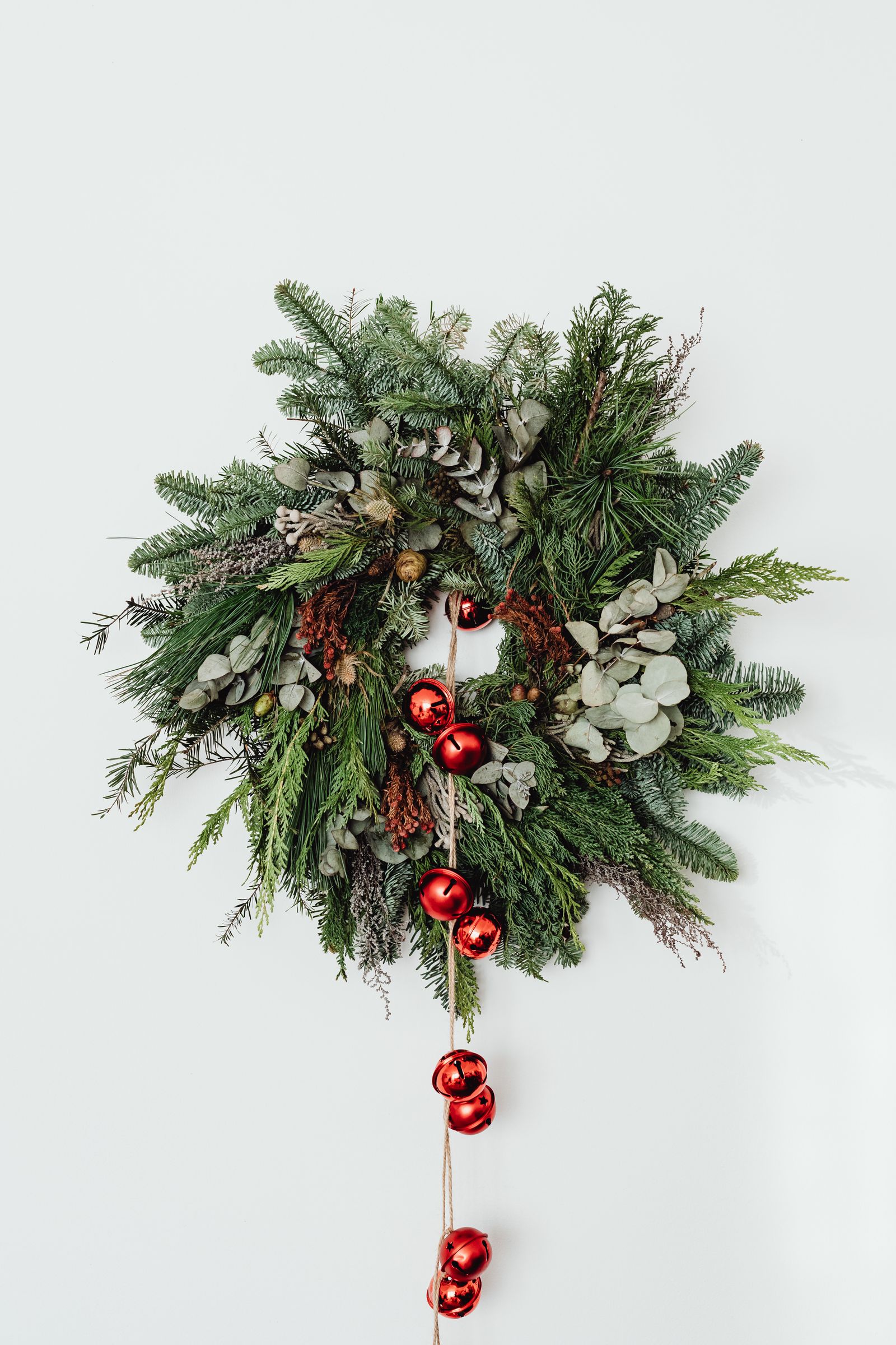 A fresh evergreen wreath with red baubles and eucalyptus on a white wall