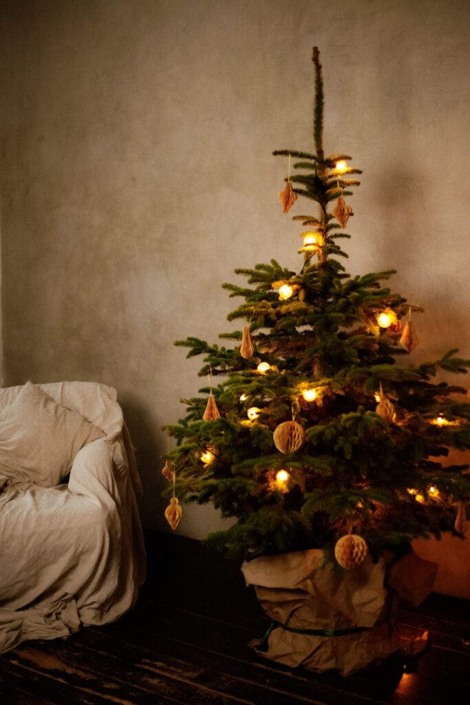 A Christmas tree with warm lights and dried orange slices beside an armchair in a living room