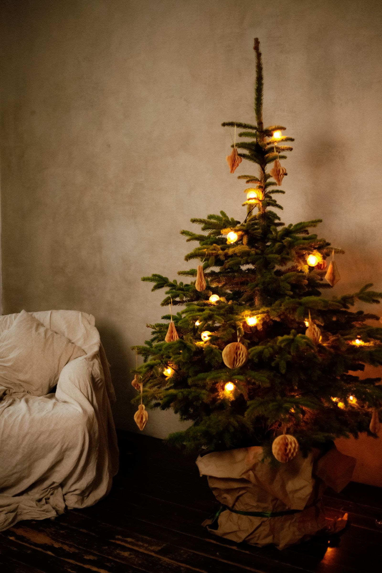 A Christmas tree with warm lights and dried orange slices beside an armchair in a living room