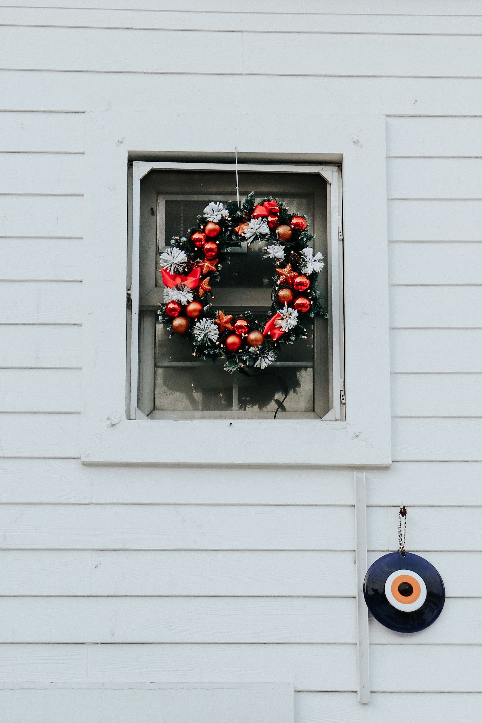 A wreath with red and silver baubles hanging in a white wooden window