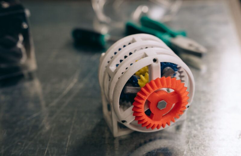 A 3D printed gear mechanism in white and orange on a metal bench