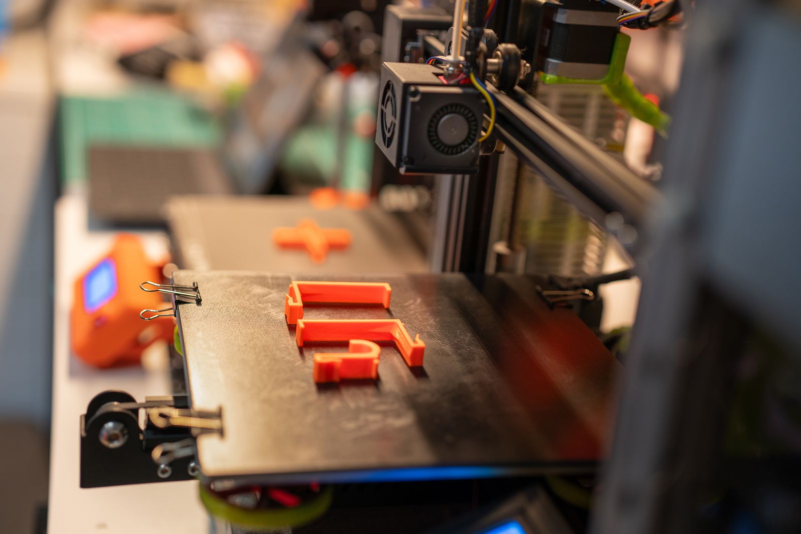 Orange 3D printed parts on the bed of a 3D printer in a workshop