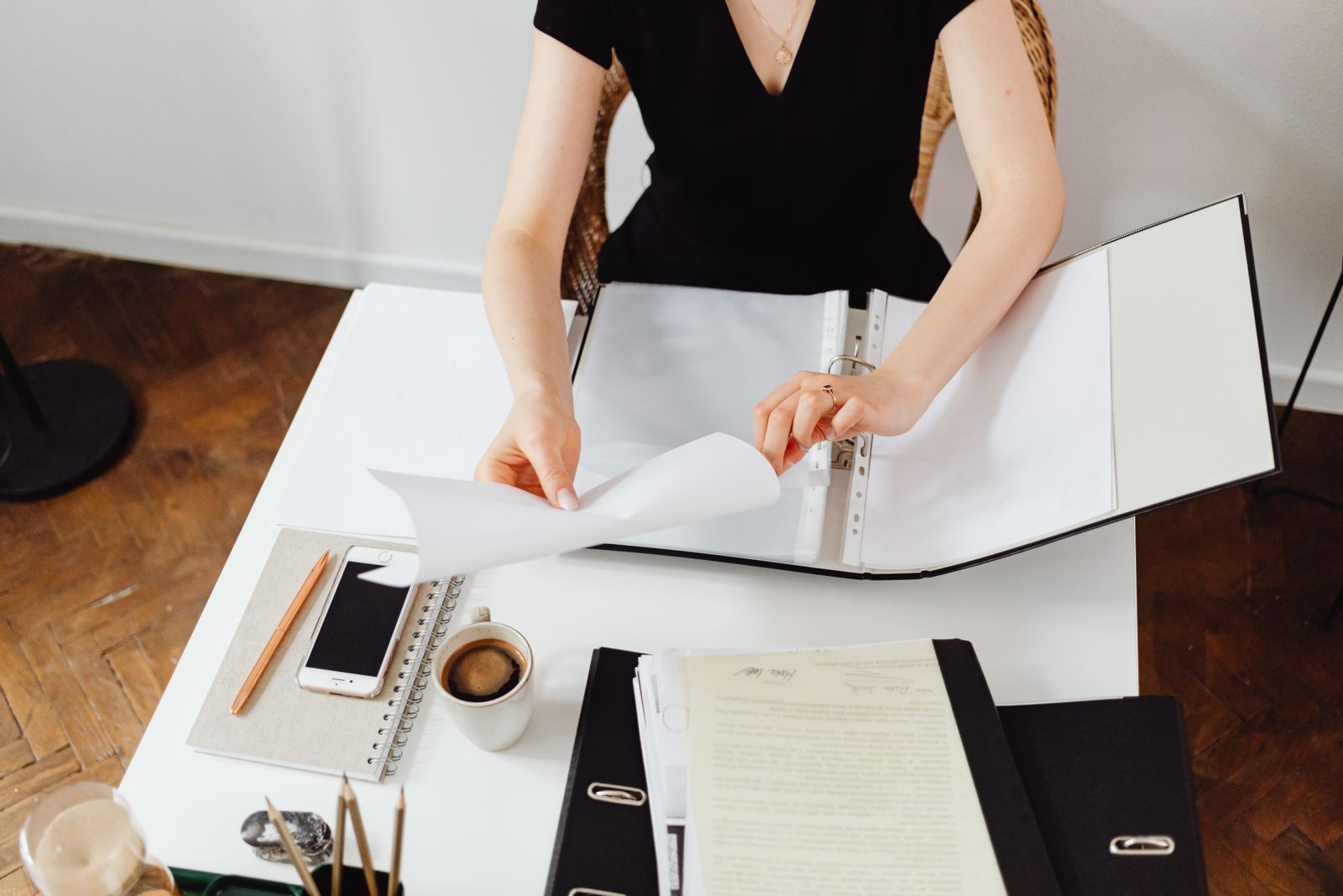 A person going through papers in a ring binder at a white desk