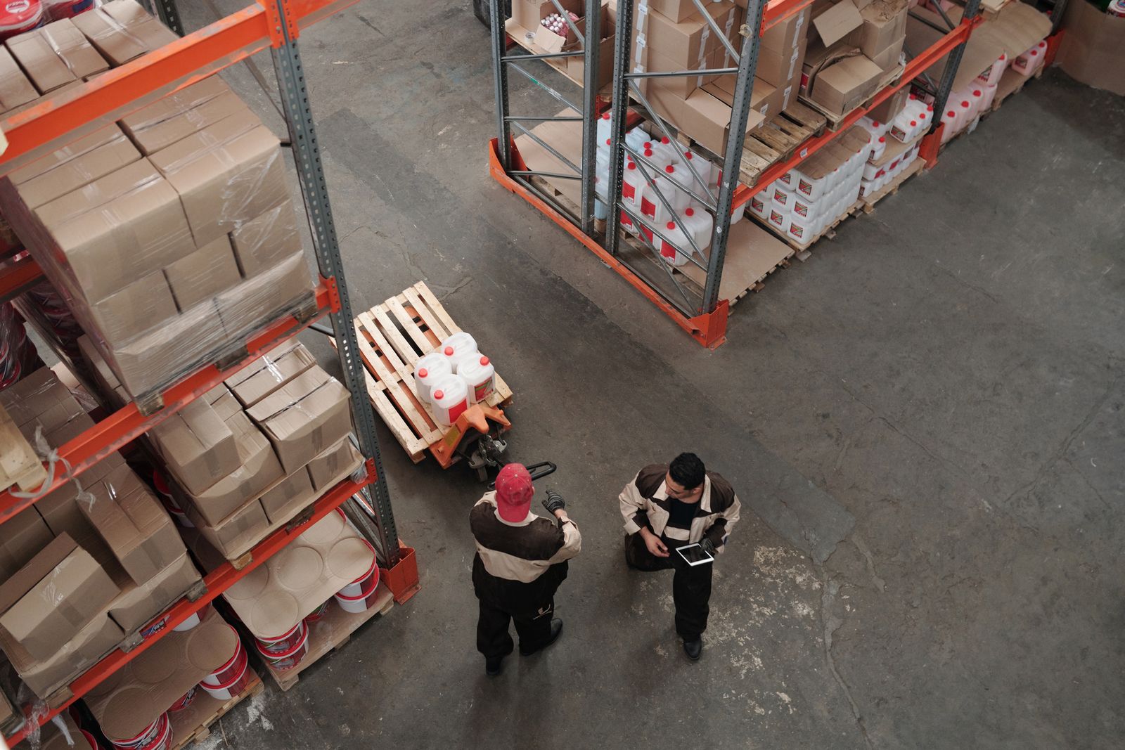 Warehouse staff moving pallets between rows of shelving, seen from above