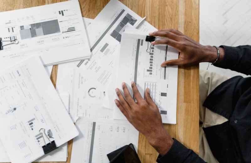 Top view of a person reviewing documents spread on a wooden desk