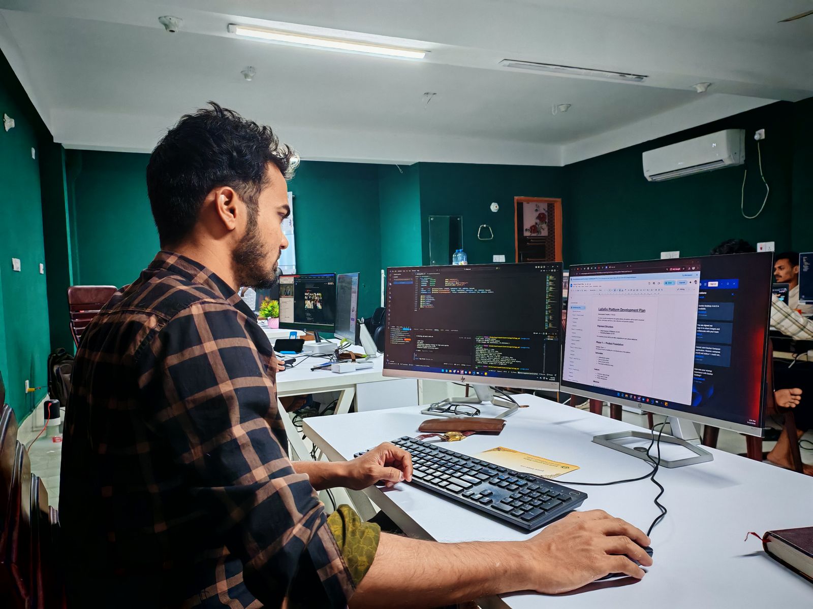 A software developer working at two monitors in a bright office