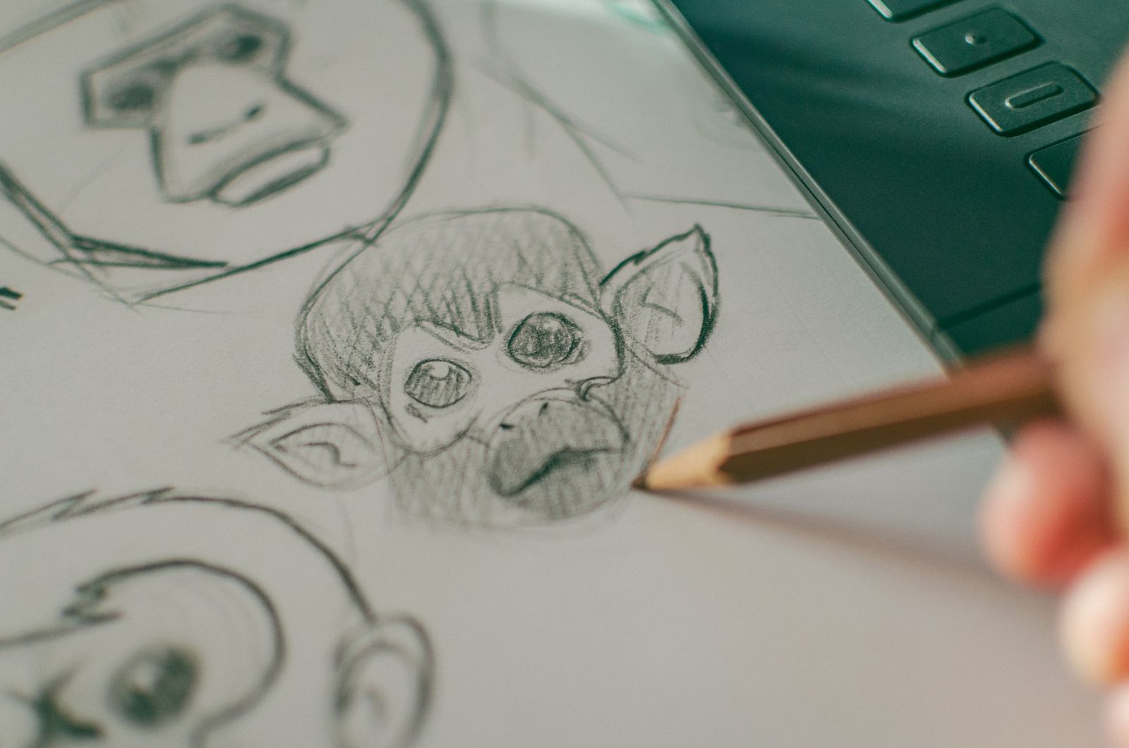 A hand sketching cartoon monkey faces in pencil