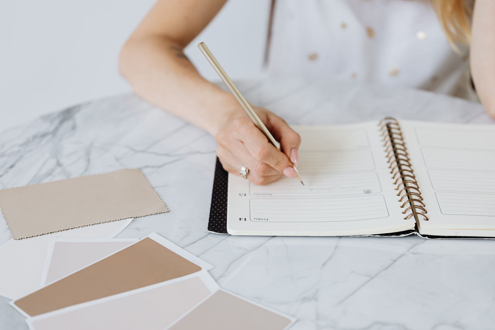 A hand writing in a ring-bound planner beside paper colour swatches