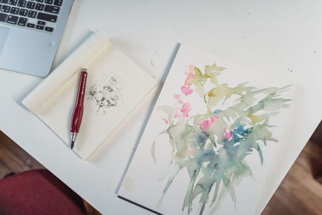 A pen beside a watercolour sketch of flowers on a white desk
